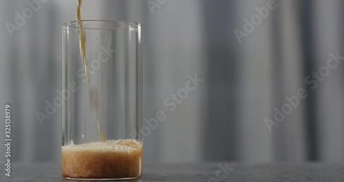 Slow motion dark beer pour into glass on concrete countertop