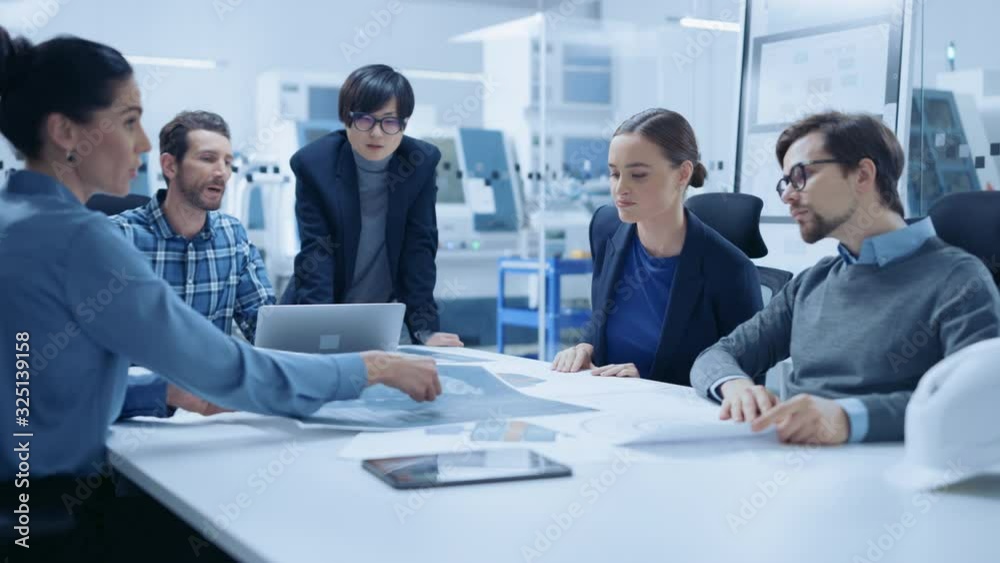 Modern Factory Office Meeting Room: Multi Ethnic and Diverse Team of Engineers, Managers and Investors Talking Sitting at Conference Table, Analyzing Blueprints. High-Tech Manufactory Optimization