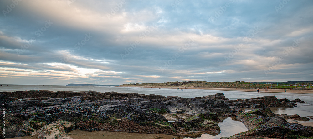 Looking across rock pools to a long beach and sand dunes