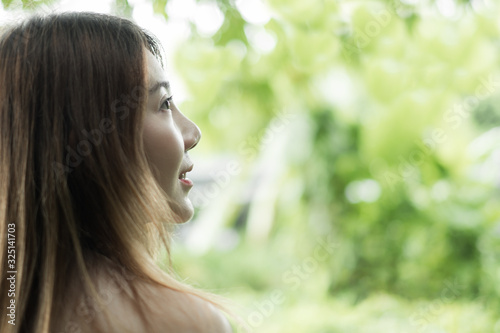 closeup portrait asian woman looking at space from behide against green tree nature background. selective focus