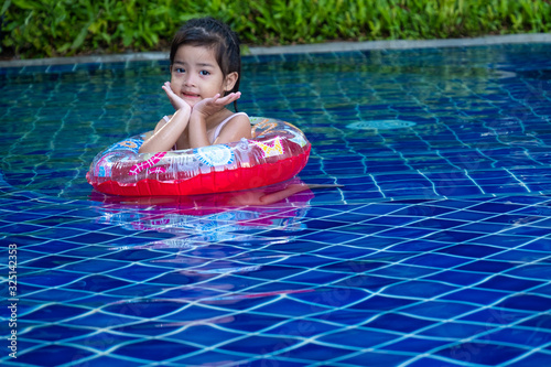 Portrait of cute little asian girl having fun and smiling in the swimming pool, floating in blue refreshing water with colurful rubber ring