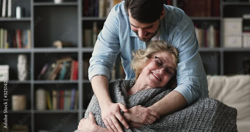 Caring grown son covering mature mother with warm plaid