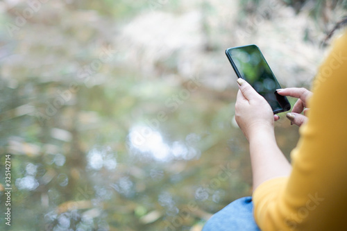 woman's hand holding and using smartphone, black screen with blur nature background. subject is blur.