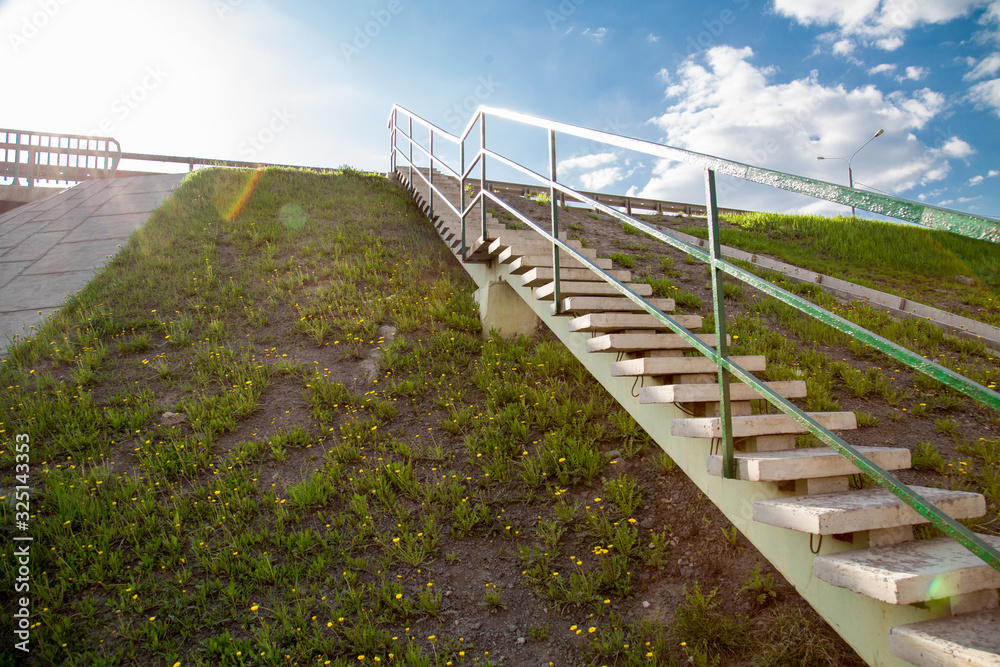 View of a concrete staircase on the slope of a road with yellow flowers on a clear Sunny day of the setting sun, construction industry.