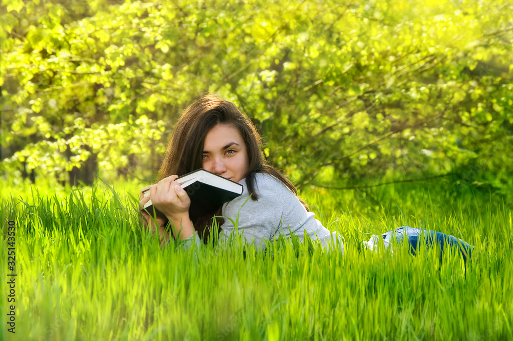 beautiful young woman girl reading a book in a park lying on the grass ...