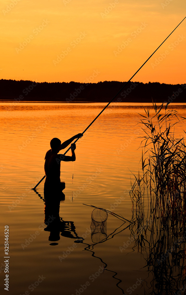 Silhouette of man fishing in water over sunset