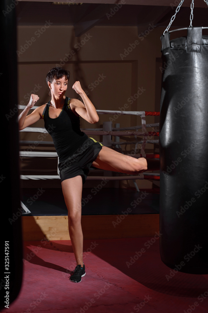 A young Caucasian woman actively trains in the gym and do boxing exercises in boxing gloves in front of a punching bag