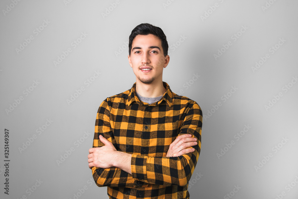 handsome looking guy in yellow square shirt with arms crossed isolated on grey background