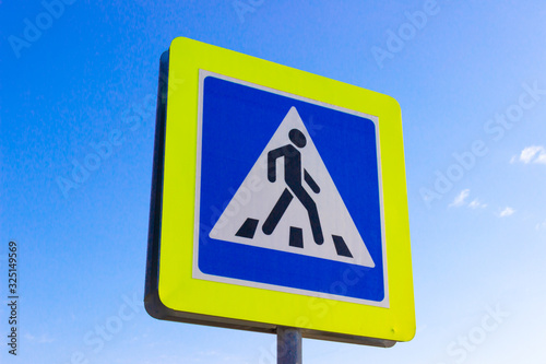 International road sign "Pedestrian crossing" on clean blue sky background Symbolic person crossing street.