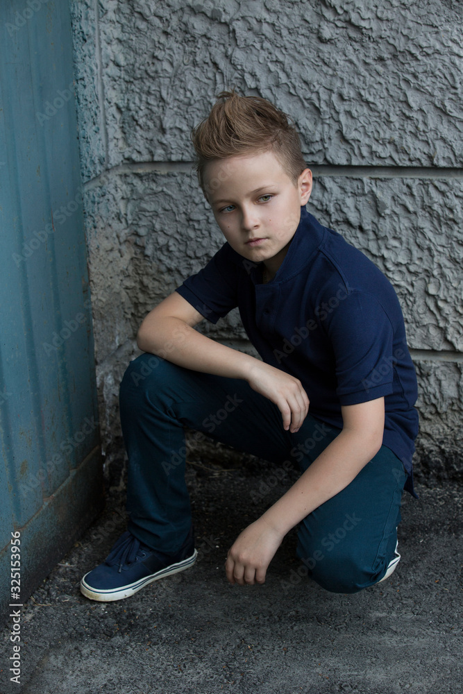 Handsome stylish boy sitting near a wall on the street. The boy has one eye blue, the other green. He is 13 years old.