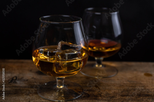 Two whiskey / cognac glasses with ice on a wooden background. Dark backdrop.