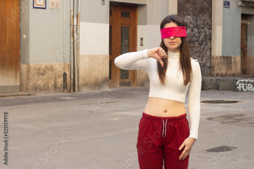 pretty  young woman with eye tape wearing a protective medical face mask, negative assessment symbol thumb down. Coronavirus, germ, mers-cov, infection, dust, air pollution, viruses, protection, conta photo