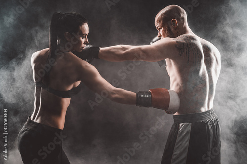 Shirtless Woman exercising with trainer at boxing and self defense lesson, studio, dark background. Female and male fight.