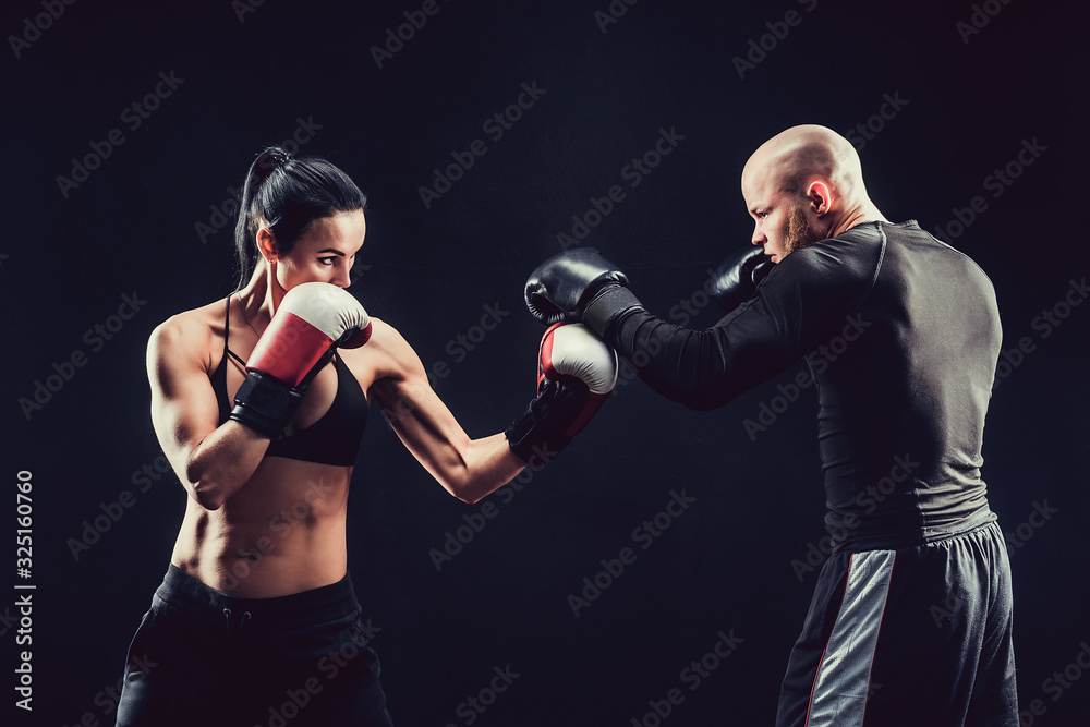 Shirtless Woman exercising with trainer at boxing and self defense lesson, studio, dark background. Female and male fight.