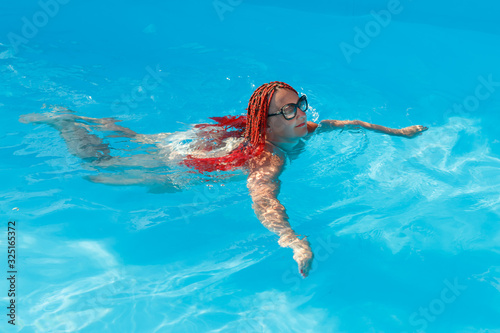 Young cheerful woman with african pigtails swims in the pool.