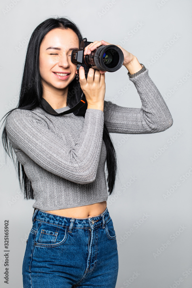 Attractive brunette aims her camera. composing a photograph in studio, isolated on gray background Attractive brunette aims her camera. composing a photograph in studio, isolated on gray background