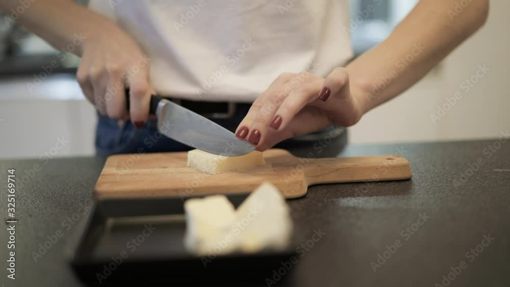 Close up of woman hands cutting fresh parmesan cheese in slices on a wodden board. Female manicured hands cutting a parmesan into sticks on a little cutting board Close up of woman hands cutting fresh parmesan cheese in slices on a wodden board. Female manicured hands cutting a parmesan into sticks on a little cutting board