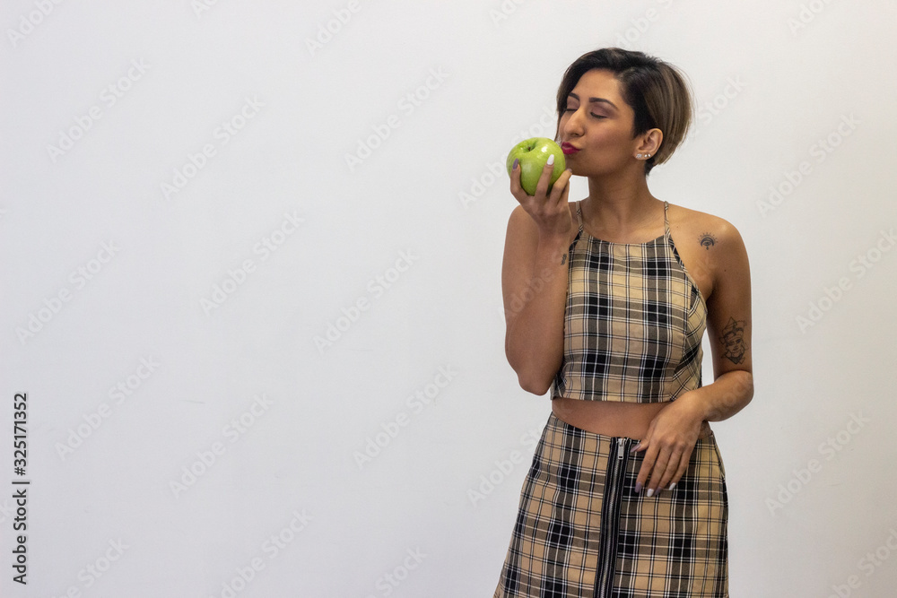 Portrait of healthy attractive latin young woman kissing an apple. Dieting concept. Healthy lifestyle with fruit, isolated on white background studio shot, plaid dress, dark air. Place for your text i Portrait of healthy attractive latin young woman kissing an apple. Dieting concept. Healthy lifestyle with fruit, isolated on white background studio shot, plaid dress, dark air. Place for your text i