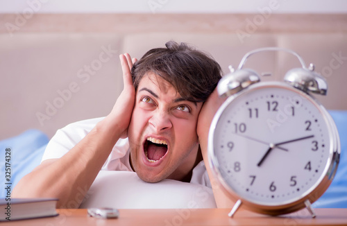 Man in bed frustrated suffering from insomnia with an alarm cloc photo