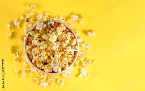 Glass bowl with salted popcorn on yellow background. Top view with copy space. Flat lay.