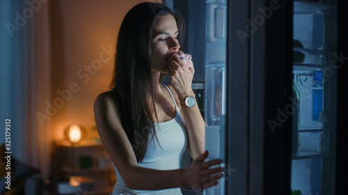 Hungry Beautiful Young Woman in the Kitchen in the Evening Opened the Fridge, Takes out a Piece of a Delicious Creamy Cake and Starting to East it. She Feels Satisfied.
