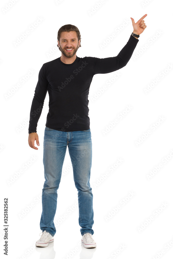 Smiling Man In Black Blouse, Jeans And Sneakers Is Pointing Up Smiling Man In Black Blouse, Jeans And Sneakers Is Pointing Up