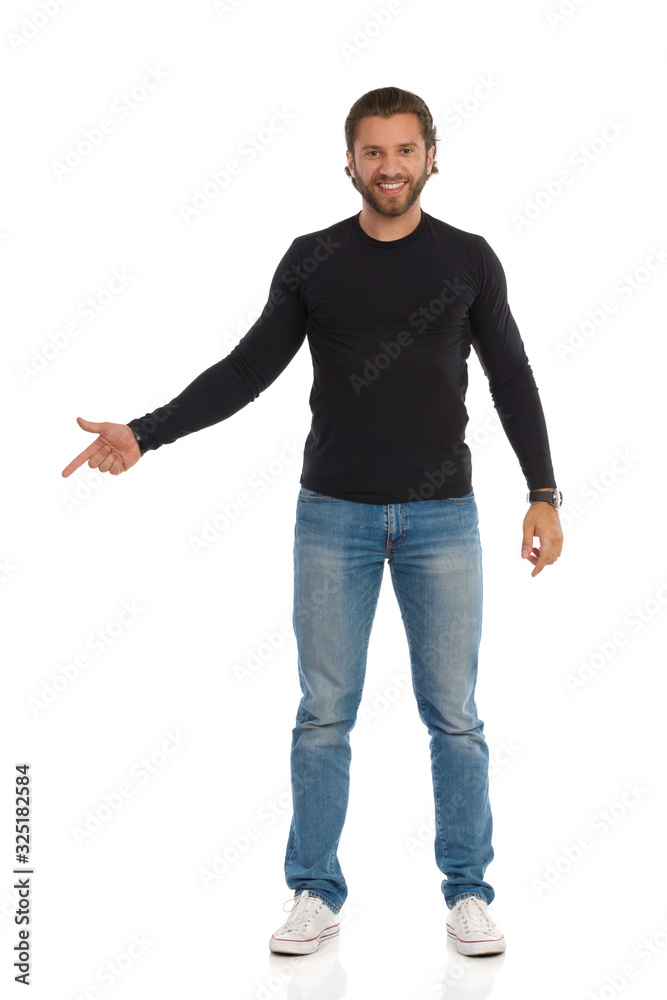 Smiling Man Is In Black Blouse, Jeans And Sneakers Is Showing Something With Index Finger Smiling Man Is In Black Blouse, Jeans And Sneakers Is Showing Something With Index Finger