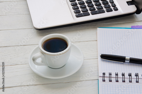 Cup of coffee, notebook with pen and laptop on white desktop