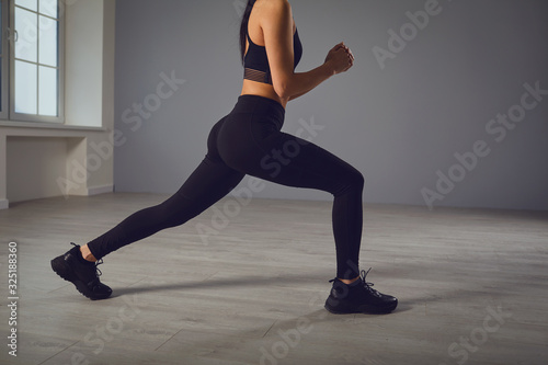 Squat exercises. Girl in black sportswear with dumbbells in her hands doing squats in a room.