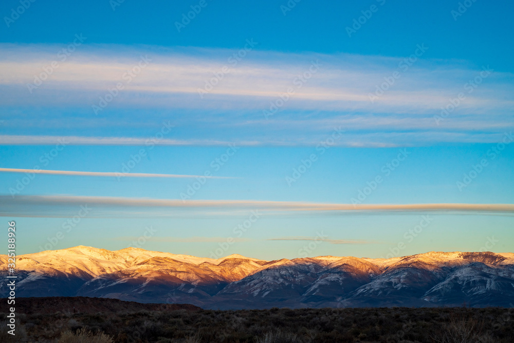 dawn light illuminates snowy Sierra Nevada mountain range streaky clouds above