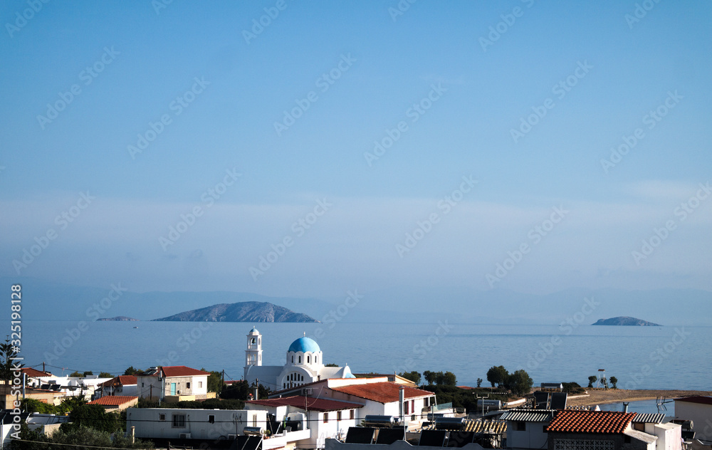 A panoramic view of the bay at the Greek island of Agistri.  In the foreground is a church. which looks out to sea to small islets and the coast of the mainland