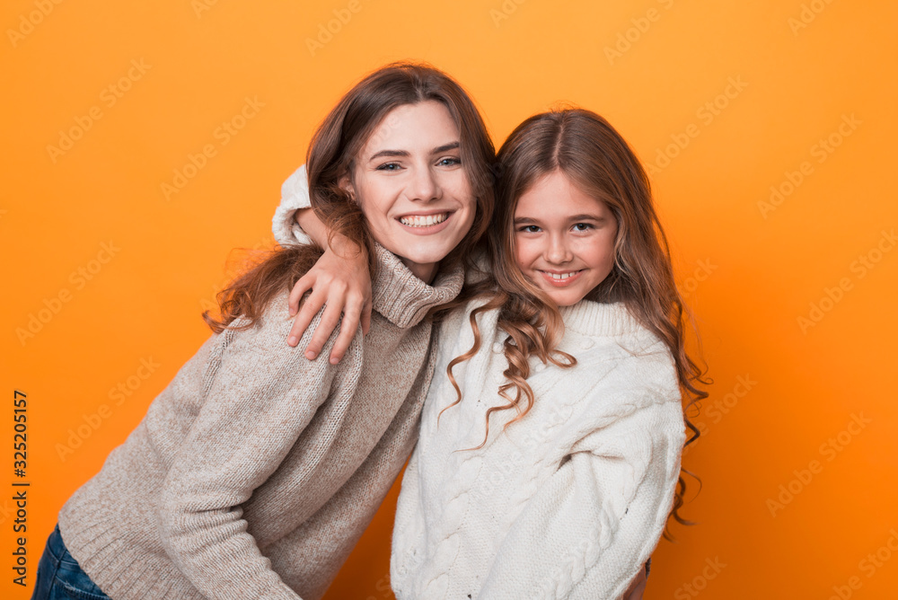 two sisters hugging and having fun in studio on orange background. age difference. two sisters hugging and having fun in studio on orange background. age difference.