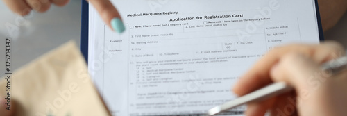 Focus on female hand holding paper folder and pointing for text. Sick patient with paper package with cannabis symbol on it and signing document. Healthcare and medical marijuana concept photo