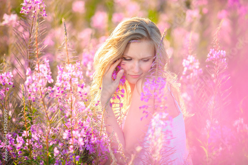 Young beautiful blonde girl gathers pink flowers in the spring blooming field at sunset. © sheikoevgeniya
