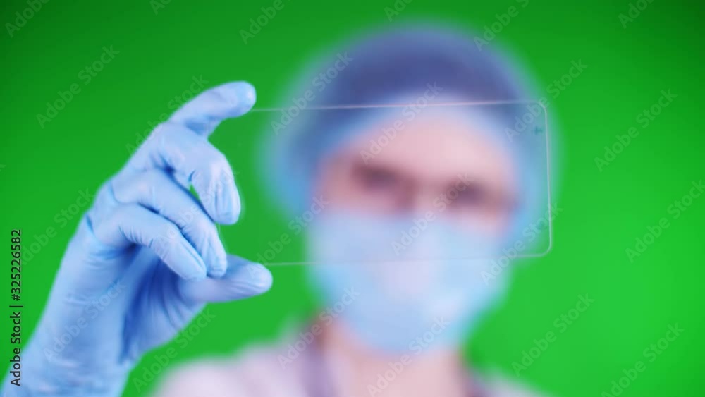 green background. close-up, doctor dressed in medical cap, mask, blue medical gloves, holds a glass card on which it is possible to place an advertisement, text or video. green background. close-up, doctor dressed in medical cap, mask, blue medical gloves, holds a glass card on which it is possible to place an advertisement, text or video.