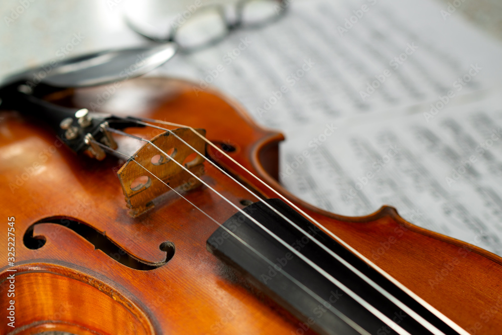 Fototapeta premium Beautiful old violin close up and eyeglasses lying on the blurred sheet music