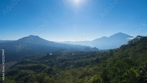 Zooming in timelapse of volcano Batur, caldera lake Batur and green woodland in front of them. Light morning clouds and brright sun. Bali, Indonesia photo