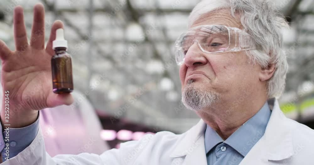 Close-up of senior grey-haired Caucasian man looking at bottle with fertilizer and turning to camera. Professional mature agronomist working in greenhouse. Cinema 4k ProRes HQ. Close-up of senior grey-haired Caucasian man looking at bottle with fertilizer and turning to camera. Professional mature agronomist working in greenhouse. Cinema 4k ProRes HQ.
