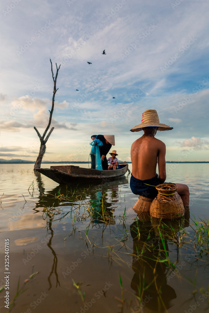 Asian boy sat in the water with fishing equipment. Father and sister aboard a fishing boat in the background.