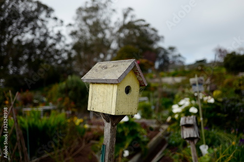 A yellow birdhouse with blurred garden in the background