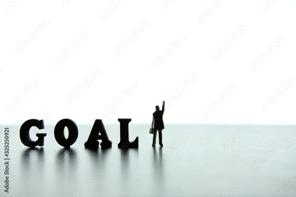 Silhouette of miniature businessmen pointing upside beside of goal word block puzzle