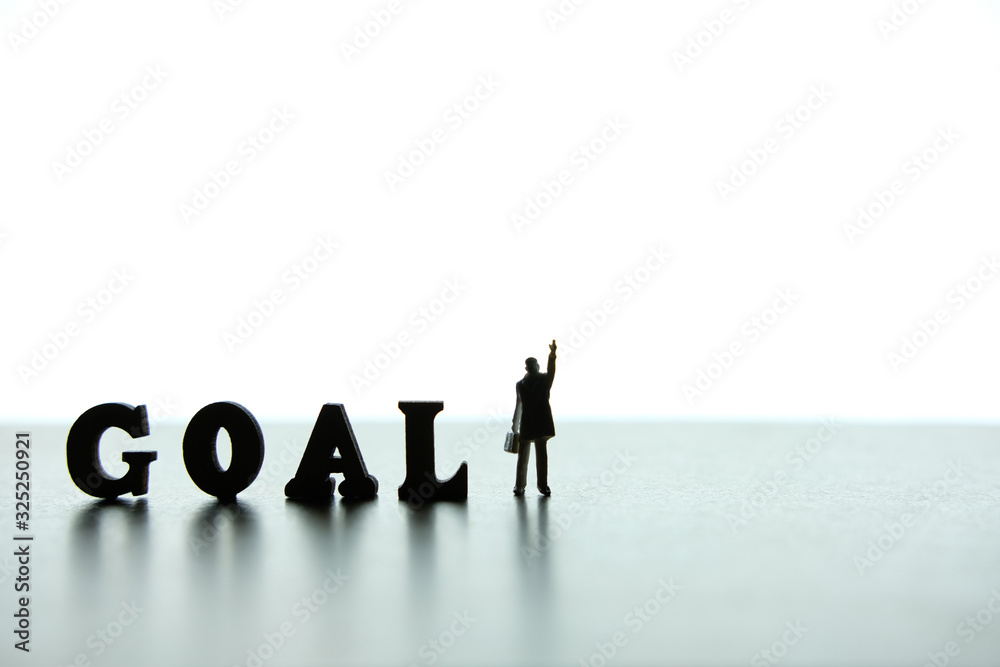 Silhouette of miniature businessmen pointing upside beside of goal word block puzzle Silhouette of miniature businessmen pointing upside beside of goal word block puzzle