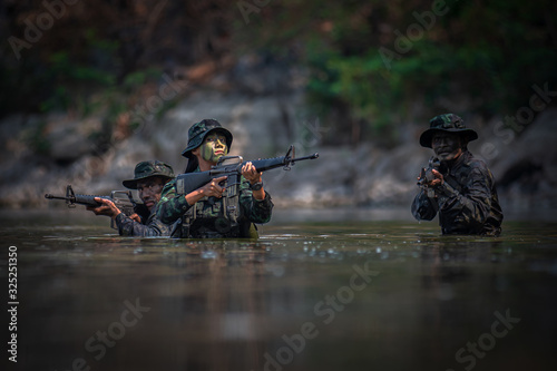 Soldiers with gun are walking along the river. War, soldier army, gun and hostage rescue concept.