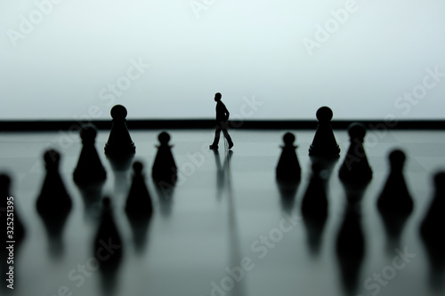 Business strategy conceptual photo - Miniature of businessman walking forward in the middle of chess piece on a chessboard 