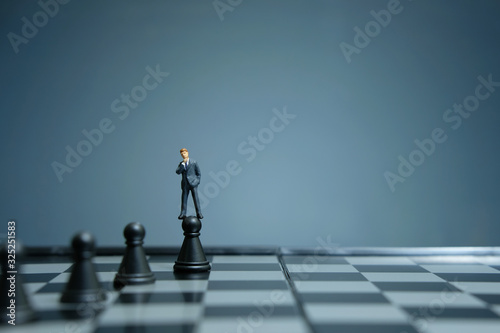 Business strategy conceptual photo - miniature businessman standing above castle pawn on a chessboard