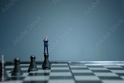 Business strategy conceptual photo - miniature businessman standing above castle pawn on a chessboard photo