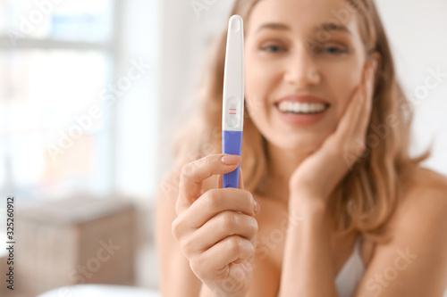 Happy young woman with pregnancy test in bathroom, closeup