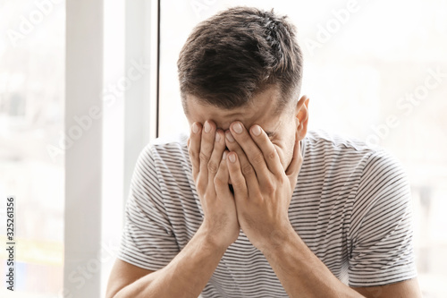 Depressed young man near window
