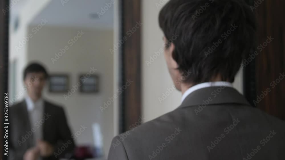 Young man dressing himself in front of mirror in suit