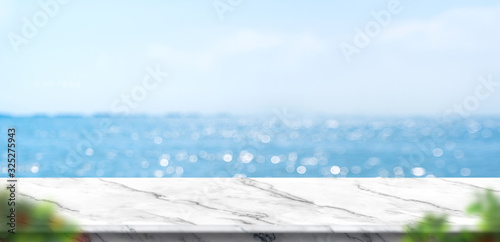 Empty white marble table with blur blue sky and sea bokeh background with green leaf foreground,Mock up template for display or montage of product or content use as banner in social media ads